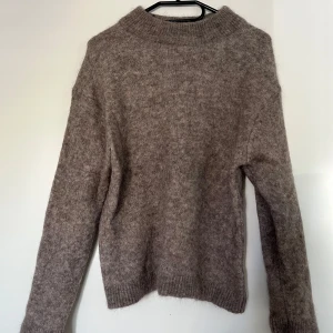 Stickad tröja, H&M, brun, XS - Brunmelerad stickad tröja med rund halsringning från H&M. Tröjan har en avslappnad passform. Storlek XS. 25% alpacka, 35% ull, 27% polyamide och 3% elastan. Mycket bra skick.   Mått: Längd ca 63 cm Byst ca 52 cm Midja ca 45 cm Ärmlängd mätt från axel ca 55 cm