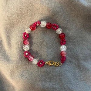 Rosa och vita pärlarmband med blommor - Jag gör egna smycken. Handgjort armband med glittriga rosa och vita pärlor, dekorerat med små blommor av rosa pärlor och guldfärgat spänne. Perfekt för dig som vill ha något färgglatt och unikt på handleden.
