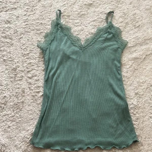 Grön ribbad linnetopp från Amisu - Supersöt ljusgrön ribbad linnetopp från Amisu med spetsdetaljer längs v-ringningen och tunna axelband. Toppen har vågig kant nertill och är perfekt för varma dagar eller lager på lager. Enkel att styla och ger en fräsch vibe till din outfit.