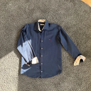 Mörkblå Burberry skjorta  - Snygg skjorta ifrån burbbery, perfekt nu till sommaren inga täcken på användning och passformen är perfekt om man utgår ifrån storlek S