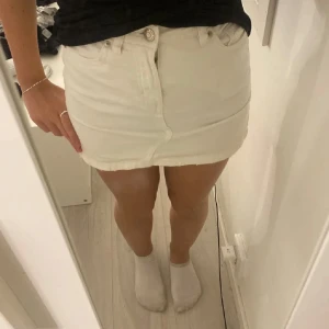 Vit jeanskjol från LAB Industries - Snygg vit jeanskjol från LAB Industries med klassisk femficksdesign och rå kant nertill. Kjolen är kort och har bälteshällor, knapp och dragkedja framtill samt bakfickor. Perfekt till sneakers eller boots för en fräsch look.