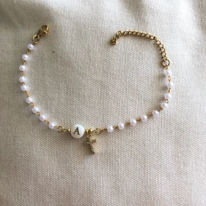 Armband med guldkjedje och pärlor med bokstaven A och kors - Snyggt armband med små vita pärlor på guldfärgad kedja. I mitten sitter en rund vit pärla med bokstaven A i guld och ett litet kors i diamanter som glittrar. Jättefin men kommer inte t användning (Inte äkta silver!)
