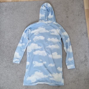 Blå molnmönstrad hoodieklänning Lindex - Köp denna Supermysiga hoodieklänningen från Lindex i ljusblått med vita moln över hela. Långärmad och med huva, perfekt för chill dagar. Tillverkad i mjuk bomull som känns skön mot huden. Snygg och unik med sitt drömmiga molnprint💓 Storleken visas på bilden! 