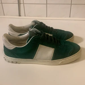 Valentino flycrew sneakers grön/vit - Snygga Valentino Rockrunner sneakers i mörkgrönt mocka och vitt skinn. Klassisk låg modell med svarta snören, vit sula och coola nitar baktill. Perfekta för dig som vill sticka ut med exklusiva detaljer och streetkänsla.