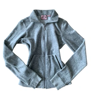 Grå ziptröja från Juicy Couture - Säljer en grå långärmad ziptröja från Juicy Couture med mjukt fleecematerial. Tröjan har hög krage, dragkedja framtill och två fickor. Perfekt för chill dagar eller när du vill ha en comfy look. Klassisk Juicy Couture-label i rosa på insidan av kragen.