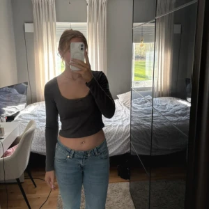 Mörkgrå croppad långärmad topp - Säljer en mörkgrå croppad topp med lång ärm och fyrkantig ringning. Toppen är tight och har en enkel, stilren look som passar perfekt till jeans eller kjol. Materialet känns mjukt och stretchigt, vilket gör den bekväm att bära hela dagen.