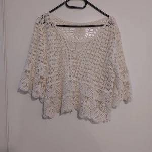Vit virkad blus i bomull - Superfin vit blus med virkad design och breda trekvartsärmar. Blusen är gjord i 100% bomull och har ett detaljerat spetsmönster med snygga vågiga kanter. Perfekt för dig som gillar boho-vibes och vill ha något luftigt och unikt.Storlek s/m.