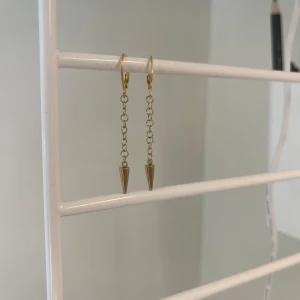 Guldiga kedjeörhängen med koner - Snygga örhängen i guld med tunn kedja och spetsig konformad detalj längst ner. Perfekta för dig som gillar minimalistisk stil med en edgy twist. Lätta att matcha med andra smycken och passar till alla tillfällen. I rostfritt stål och handgjort 