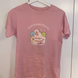 Rosa Sumikko Gurashi t-shirt Uniqlo - Söt rosa t-shirt från Uniqlo med Sumikko Gurashi-tryck framtill. Motivet visar gulliga figurer runt en jordgubbstårta. Mycket bra skick!!
