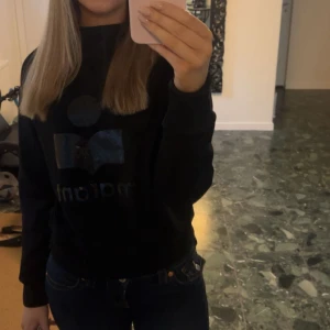 Svart sweatshirt från Isabel Marant Étoile - Cool svart sweatshirt från Marant Étoile med glansigt logotryck framtill. Tröjan har rund hals, långa ärmar och ribbade muddar vid ärmslut och nederkant. Perfekt till jeans eller cargo pants för en chill vibe.
