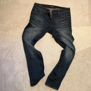 Jack & Jones jeans - Tim - Snygga mörkblå jeans från Jack & Jones med klassisk femficksdesign och bruna sömmar. Jeansen har en straight/slim passform och är tillverkade i slitstarkt denim med lätt tvättad look. Perfekt för dig som gillar stilrena och tidlösa jeans.