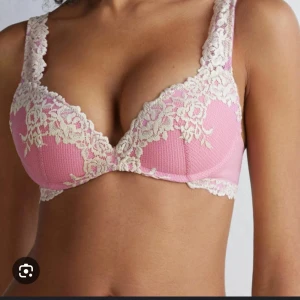 Rosa spetslinnetopp med blommönster - Supersöt rosa linnetopp med krämvit spets och blommigt mönster. Toppen har vadderade kupor och breda axelband med spetsdetaljer. Perfekt för dig som vill ha en feminin och romantisk vibe på din outfit.