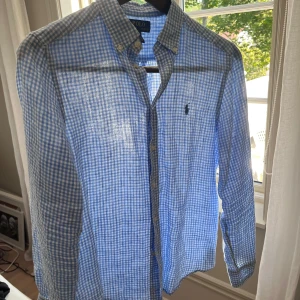Blårutig linneskjorta från Polo Ralph Lauren - Snygg blårutig skjorta från Polo Ralph Lauren med klassisk button-down krage och broderad logga på bröstet. Skjortan har långa ärmar, vita knappar och är gjord i 100% linne som passar perfekt till varma dagar. Fräsch och stilren look.