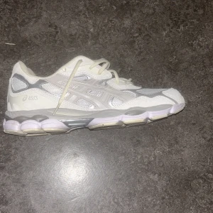 Vita Asics sneakers med mesh och skinn - Säljer ett par fräscha vita Asics sneakers med coola detaljer i silver och grått. Skon har meshpaneler för extra ventilation och inslag av skinn för en snygg look. Platt sula och snörning gör dem både bekväma och stilrena. Perfekta för dig som gillar sportig vibe.