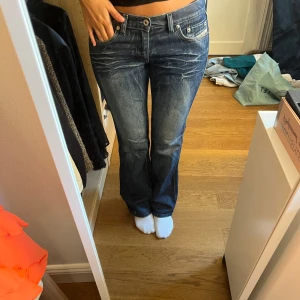 Diesel bootcut jeans blå - Säljer ett par snygga blå jeans från Diesel med bootcut passform och klassisk femficksdesign. Jeansen har ljusa slitningar framtill och en liten röd  diesel logga på fram och på bakfickan. De är midwaist och tillverkade i mjukt jeansmaterial med lite stretch för skön passform.
