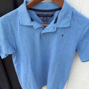 Blå piké t-shirt Tommy Hilfiger - Snygg blå piké t-shirt från Tommy Hilfiger med klassisk krage och korta ärmar. T-shirten har ett litet broderat Hilfiger-logo på bröstet och är gjord i mjuk bomull. Perfekt för dig som gillar stilren och enkel design.