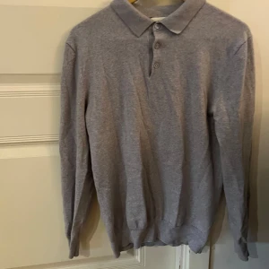 Grå pikétröja från John Henric - Snygg grå pikétröja från John Henric i storlek M. Tröjan har klassisk krage, tre knappar framtill och är långärmad. Materialet är mjukt och stickat, perfekt för dig som gillar stilrena och enkla plagg. Passar M/S. Tröjan är ganska liten för M och är mer S.