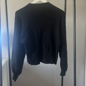 Svart stickad tröja med lång ärm - En svart stickad tröja med rund hals och långa ärmar, med en liten krage.Mjuk och skön känsla, passar dig som gillar stilrena plagg.