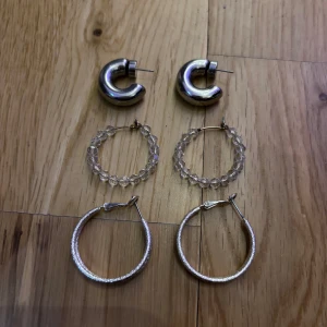 Tre par coola örhängen i silver och glas - Säljer tre par örhängen: chunky silvriga hoops med rundad form, ett par glittriga hoops med transparenta pärlor och ett par tunna silvriga hoops med textur. Perfekt för dig som gillar att mixa stilar och vill ha något som sticker ut. Använd men i mycket bra skick 