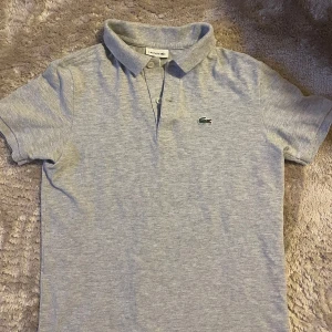 Grå pikétröja från Lacoste - Snygg grå pikétröja från Lacoste. Felfri, utan noppor. 