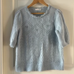 Ljusblå stickad Odd Molly tröja - Superfin ljusblå stickad tröja från Odd Molly med korta puffärmar och vacker spetskant vid halsen. Tröjan har ett detaljerat hålmönster med blommiga inslag och ribbad nederkant. Perfekt för dig som gillar romantisk och feminin stil.
