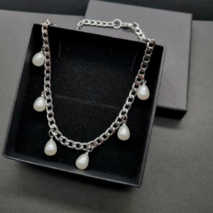 Silverhalsband med droppformade pärlor - Stilrent halsband i silverfärgad metall med chunky kedja och sju droppformade vita pärlor som hänger längs hela kedjan. Perfekt för dig som vill ha en cool och modern vibe med en touch av klassisk pärlfeeling.