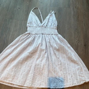 Ljus blå omlottklänning med smock från SHEIN  - Söt ljus blå kortklänning med omlott och smock i midjan. Klänningen har tunna axelband och v-ringad hals, samt ett subtilt randigt mönster i tyget. Materialet känns lätt och luftigt, perfekt för varma dagar. Passformen är normal och kjolen är utställd för en flowy vibe.