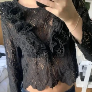 Svart spetsblus med volangdetaljer - Supersnygg svart blus i spets med genombrutet mönster och volangdetaljer framtill. Från Zara, perfekt till hösten!