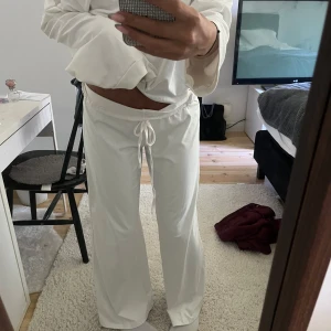 Vitt mys-sett - Säljer ett par vita mjukisbyxor med breda ben och snörning i midjan. Byxorna har låg midja och är tillverkade i ett mjukt och skönt material som passar perfekt för chill dagar hemma. Stilen är loose och de har en enkel, clean look. Tröjan är offshoulder.