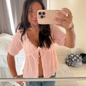 Ljusrosa stickad blus med knyt - Superfin ljusrosa stickad blus med korta ärmar och v-ringning. Blusen har ribbad struktur och ett sött knyt framtill som ger en chill och feminin vibe. Perfekt att styla med jeans eller kjol för en söt look.