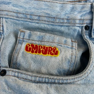 Ljusblå jeans med broderad ficka - Säljer ett par ljusblå jeans med coolt broderi i rött och gult på myntfickan. Jeansen har klassisk femficksdesign och raka ben. Perfekt för dig som gillar streetwear och vill sticka ut med detaljer. Materialet är slitstarkt denim.