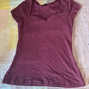 Ribbad vinröd topp från Anna Field - Snygg vinröd topp från Anna Field med ribbad struktur och korta ärmar. Toppen har en v-ringad sweetheart-krage som ger en cool och feminin vibe. Perfekt att styla med jeans eller kjol för en trendig look. Tröjan är i storlek s. För mer frågor är det bara att dma💕