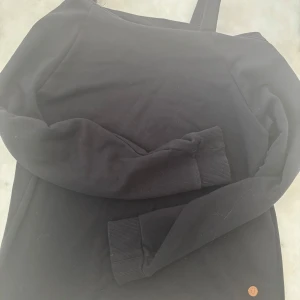 One shoulder tröja  - Svart hoodie från U i storlek 158/164. Tröjan har one shoulder och långa ärmar med ribbade muddar. Perfekt för chill dagar och enkel att matcha med jeans eller mjukisbyxor. Materialet känns mjukt och bekvämt mot huden.