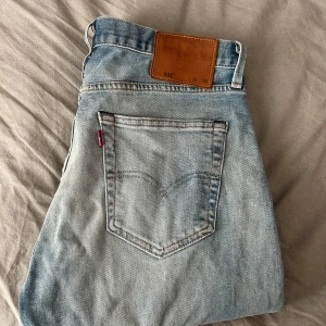 Levi's 501 ljusblå jeans straight fit - Säljer ett par klassiska Levi's 501 jeans i ljusblå tvätt med raka ben och knappgylf. De har den ikoniska läderpatchen bak och röd Levi's-tag på bakfickan. Perfekt för dig som gillar tidlös stil och vill ha ett par jeans med snygg passform.