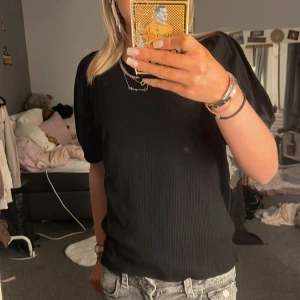 Svart ribbad topp från Object - Säljer en stilren svart ribbad topp från Object. Toppen har korta puffärmar och en rund halsringning. Perfekt för en chic och enkel look. Passar bra till både jeans och kjol.