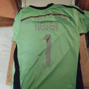 Neuer 2014 world champions  - Säljer en grön fotbollströja från Adidas med svarta detaljer och FIFA 2014 world champions-märke på bröstet. Tröjan har korta ärmar och nummer 1 på ryggen.