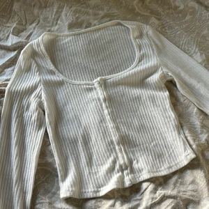 Vit ribbad topp - Säljer en stilren vit ribbad topp med långa ärmar och knäppning framtill. Säljer för den aldrig kommer till användning💕 helt i nyskick