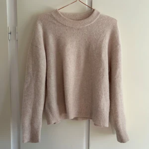 Stickad tröja - Mysig beige/ljusrosa stickad tröja med rund hals och långa ärmar. Perfekt för kyliga dagar och enkel att matcha med jeans eller kjol. Tröjan har ribbade muddar vid ärmslut och nederkant för en stilren look.