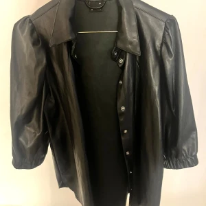 Svart skinntröja/kofta  - Snygg svart skinntröja/kofta med trekvartsärm och knappar framtill. Jackan har en  krage och elastiska ärmslut 🖤