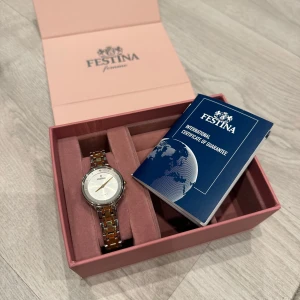 Festina damklocka i silver och guld - Elegant Festina damklocka med en stilren urtavla i silver och ett armband i en kombination av silver och guld. Klockan har en kvartsrörelse och kommer i en fin rosa förpackning med garantibevis.