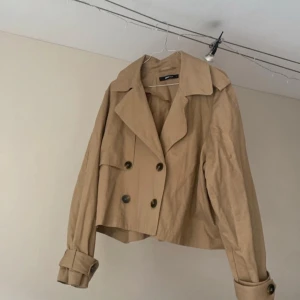 Beige kort trenchcoat Gina Tricot  - Jättefin kortare trenchcoat från Ginatricot. Storlek L men sitter jättesnyggt på mig som vanligtvis har S.   Bara använd ett fåtal gånger och i mycket bra skick. Fått så mycket komplimanger när jag haft den!!