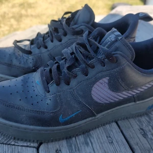 Svarta Nike Air Force sneakers - Säljer ett par klassiska svarta Nike Air Force sneakers med snörning. Skorna har en stilren design med den ikoniska Nike-loggan på sidan och en robust sula för extra komfort. Perfekta för en avslappnad stil.