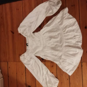 Vit klänning från Bik Bok - Säljer en söt vit klänning från Bik Bok med långa ärmar och smockdetaljer vid midjan. Perfekt för en stilren look. 💫