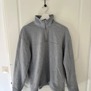 Grå tröja med dragkedja - Säljer en stilren grå tröja med dragkedja i halsen. Perfekt för en avslappnad look. Tröjan har långa ärmar och en hög krage som ger extra värme. Passar bra till både jeans och träningsbyxor.