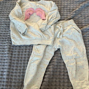 Vit och rosa prickig tröja och byxa - Säljer ett set med en vit långärmad tröja och matchande byxor. Tröjan har ett sött rosa mönster framtill och båda plaggen är dekorerade med små rosa prickar. Perfekt för en mysig dag hemma eller en avslappnad utflykt.