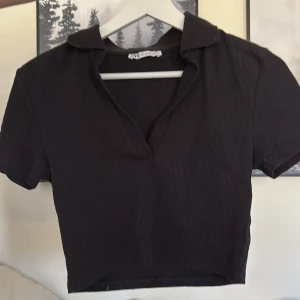 Svart ribbad polotopp från Zara - Säljer en svart ribbad polotopp från Zara. Toppen har korta ärmar och en stilren krage. 