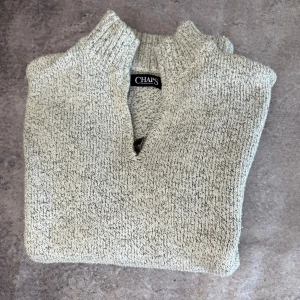 Beige stickad tröja från Chaps - Säljer en stilren beige stickad tröja från Chaps. Tröjan har en ribbad krage och en liten v-ringning. Perfekt för kyligare dagar och ger en avslappnad men ändå snygg look.