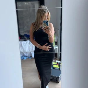 Svart långklänning med slits - Elegant svart långklänning med smala axelband och en stilren slits på sidan. Perfekt för en kväll ute eller en speciell tillställning.