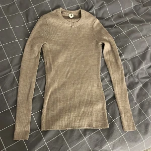 Beige ribbad tröja - Säljer en stilren beige ribbad ull-tröja med lång ärm från Arket. Tröjan har en rund halsringning och sitter tajt men är väldigt stretchig. Tröjan har även tumhål längst ner på vardera ärm. Storlek S men passar allt från XS-M då den är så pass stretchig.