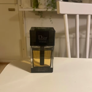 Dior Homme Intense Parfym - Säljer en elegant Dior Homme Intense parfym. Flaskan har en stilren design med en svart fyrkantig kork och genomskinligt glas som visar den gyllene vätskan. Perfekt för den som vill ha en sofistikerad doftupplevelse. Nästan använd ingenting. Kommer i förpackning. Hör av dig vid frågor!